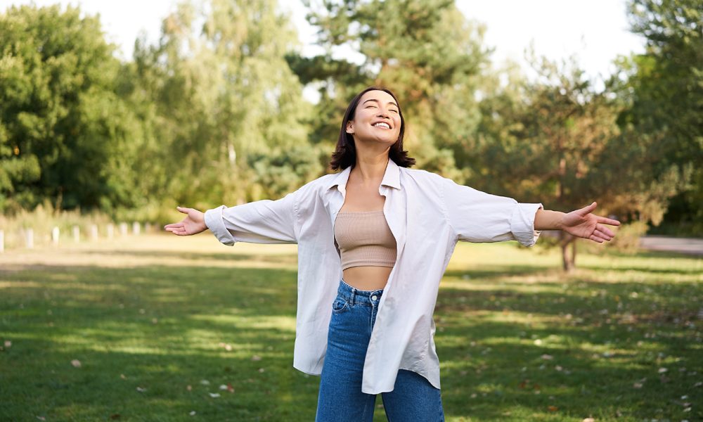 Mujer riendo disfrutando de un día soleado en el parque con los brazos estirados