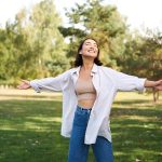 Mujer riendo disfrutando de un día soleado en el parque con los brazos estirados