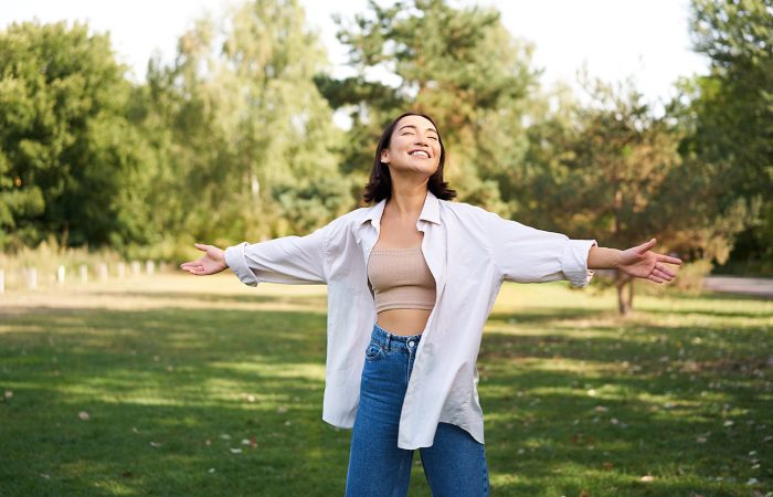 Mujer riendo disfrutando de un día soleado en el parque con los brazos estirados